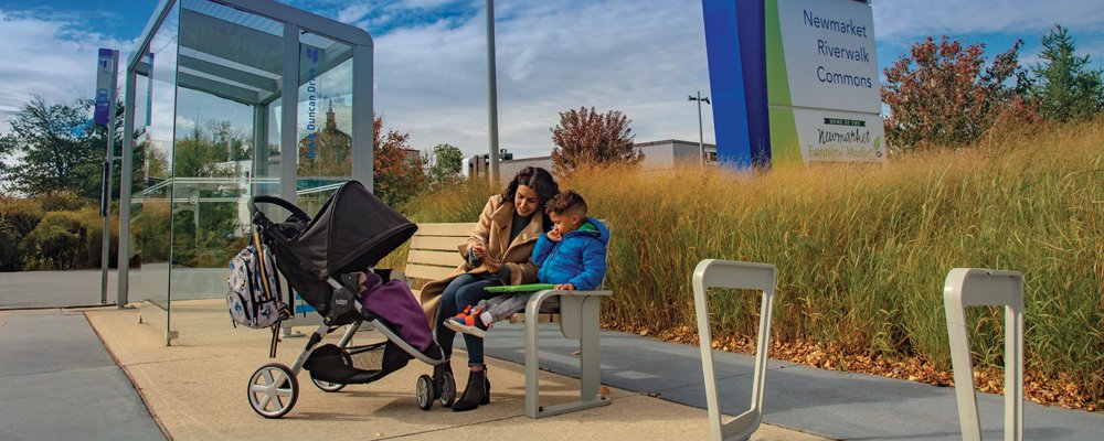 a family sitting on a bench with a stroller near a bus shelter