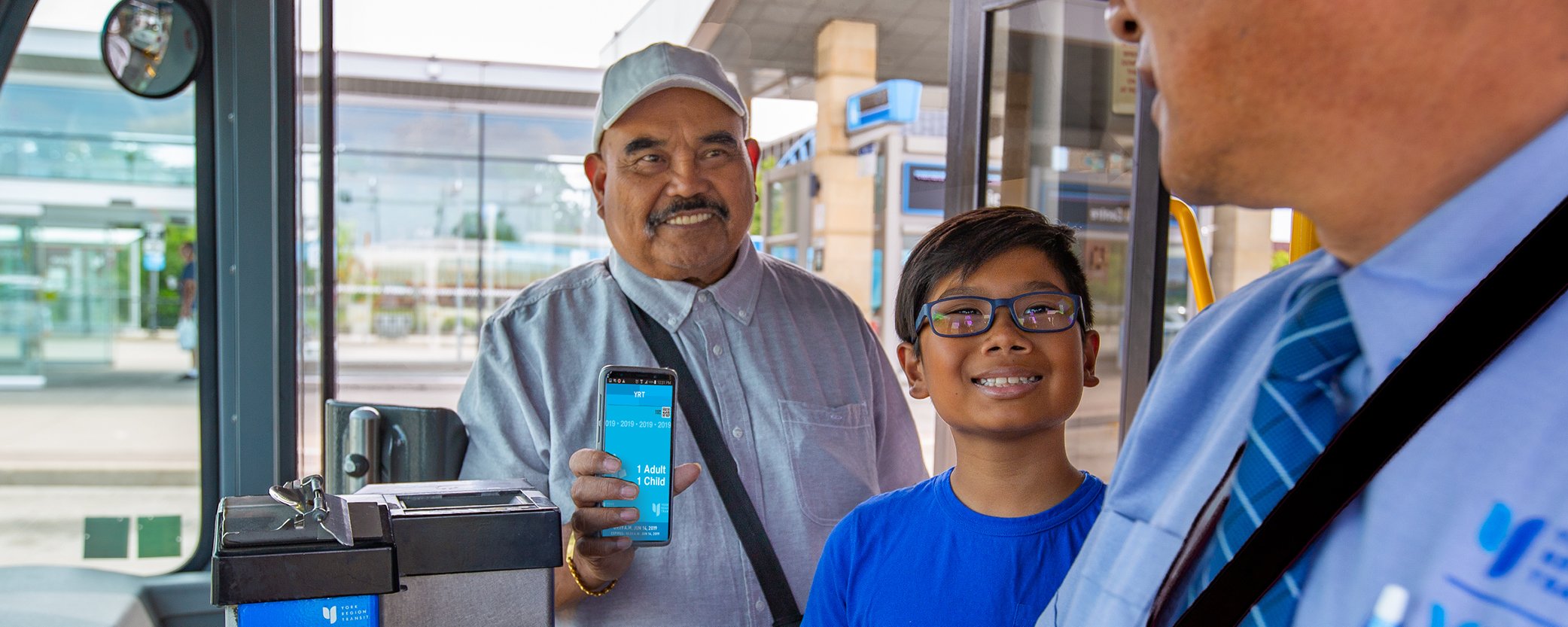 Photo of a senior with his grandson showing the bus driver proof of payment on the YRT Pay app.